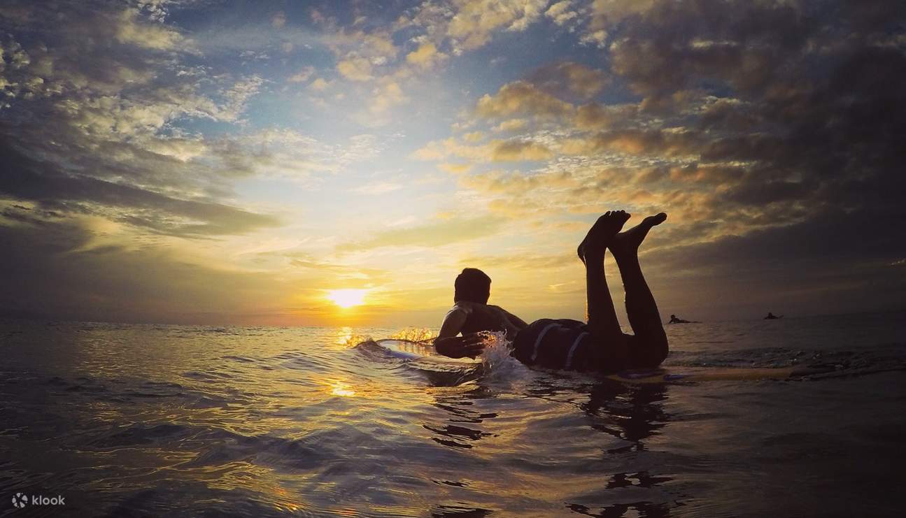 un chico mirando la puesta de sol mientras está en una tabla de surf
